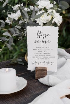 a table topped with white flowers next to a candle and a sign that says those we love