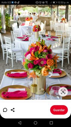 the table is set with white linens, pink and orange flowers in a vase