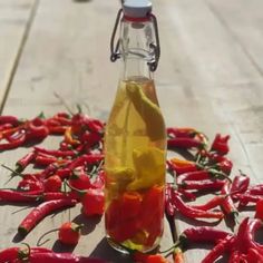 a bottle filled with yellow liquid sitting on top of a wooden table next to red peppers