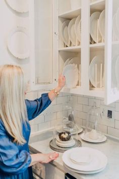 a woman standing in front of a kitchen counter with plates on it