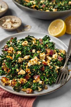 a white plate topped with spinach salad next to a bowl of lemon wedges