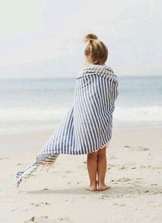 a person standing on the beach with a towel wrapped around their shoulders and looking at the ocean