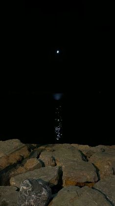 the moon shines brightly in the dark sky over some rocks and water at night