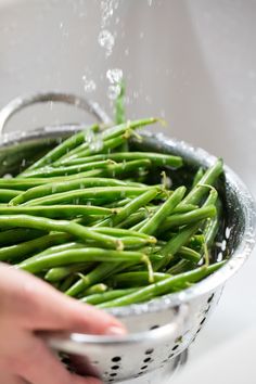 someone is sprinkling green beans in a colander