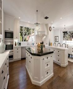 a large kitchen with white cabinets and black counter tops, an island in the middle