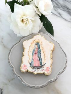 a cookie decorated with an image of the virgin mary is on a plate next to flowers