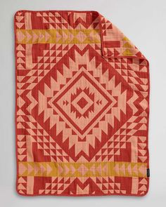 an orange and yellow blanket on top of a white surface with a red design in the middle