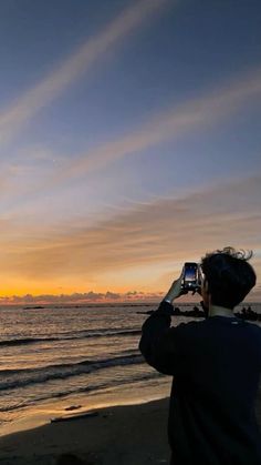 a man is taking a photo on the beach at sunset