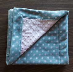 a blue and white blanket laying on top of a wooden table next to a piece of cloth