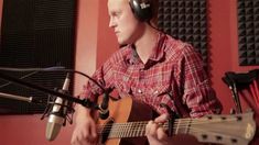 a man with headphones on playing an acoustic guitar in front of a microphone and recording equipment