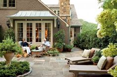 two people sitting on chairs in front of a house with potted plants and trees