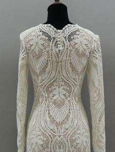 the back of a white dress with an intricate lace pattern on it and long sleeves