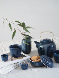 a table topped with blue dishes and cups next to a vase filled with flowers on top of a bed