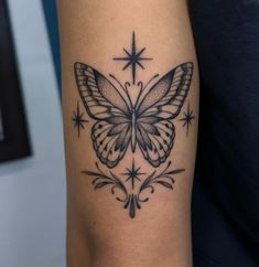 a black and white butterfly tattoo on the right arm, with stars around it's wings