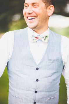 a man wearing a bow tie and vest smiling at the camera with his hands in his pockets