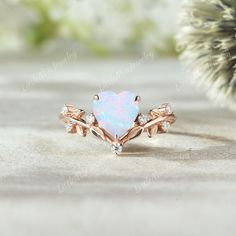 an opal and diamond ring sits on a table next to a pine tree branch