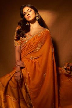 a woman in an orange sari poses for a photo with her hand on her hip