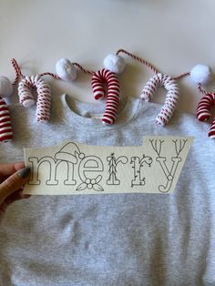 someone is holding up a t - shirt with the word merry on it and some candy canes