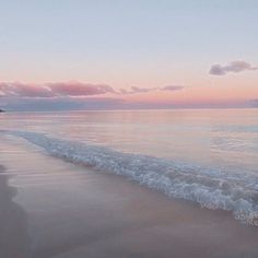 an ocean beach with waves coming in to the shore and pink clouds above it at sunset