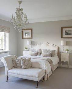 a white bed sitting in a bedroom next to a window and a chandelier