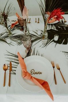 the table is set with orange napkins, silverware and palm leaves on it