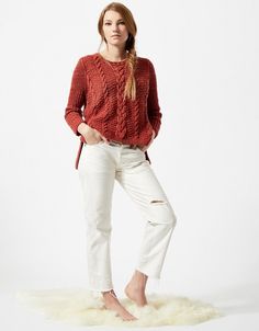 a woman standing on top of a sheepskin rug wearing a red sweater and white pants