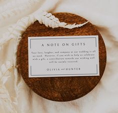 a note on gifts sitting on top of a wooden plate next to a white feather