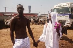 a man and woman holding hands walking in front of a truck with cows behind them