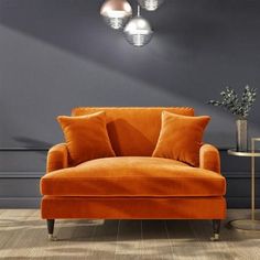 an orange couch sitting on top of a wooden floor next to a table and lamp