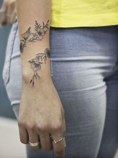 a woman's hand with a flower tattoo on her left wrist and the other arm