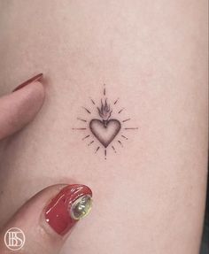 a small heart tattoo on the back of a woman's left thigh, with a sunburst above it