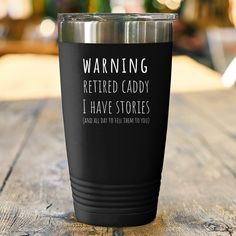 a black tumbler cup sitting on top of a wooden table with the words warning retired caddy i have stories printed on it