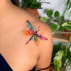 a colorful dragonfly tattoo on the back of a woman's shoulder