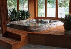 a large hot tub sitting on top of a wooden platform next to a window and potted plant