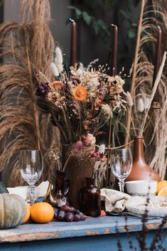 an arrangement of flowers, candles and wine glasses on a table in front of pumpkins