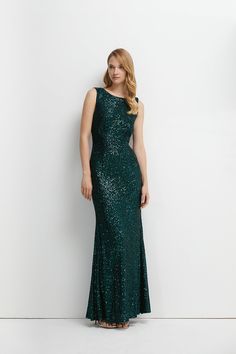 a woman in a long green sequin dress standing against a white wall with her hands on her hips