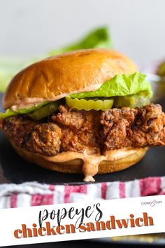 a chicken sandwich with lettuce and pickles on a black plate next to a red and white napkin