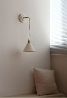 a white lamp hanging from the side of a wall next to a pillow on a bed