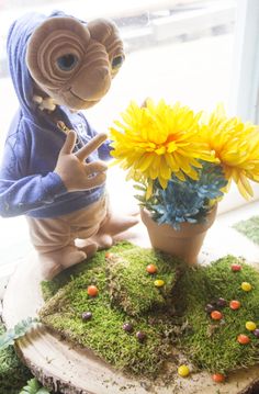 a stuffed animal sitting on top of a moss covered table next to a potted plant