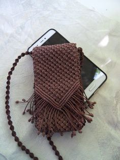 a cell phone laying on top of a brown knitted bag next to a chain