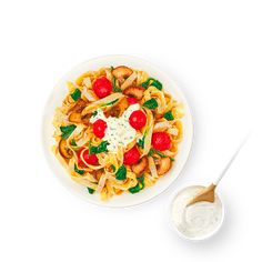 a white bowl filled with pasta and vegetables next to a small bowl of ranch dressing