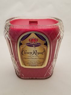 a pink candle in a clear container on a white surface with the label crown royal