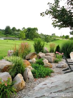 a bench sitting on top of a lush green field next to rocks and flowers in the grass