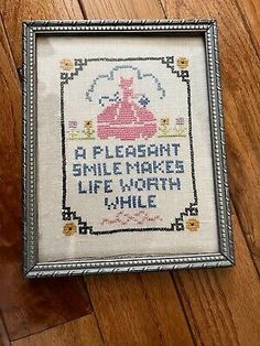 a cross stitch sample in a frame on a wooden floor with the words, i pleasant smile