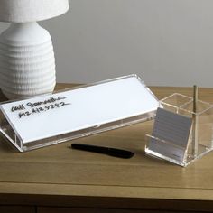 a desk with a pen, notepad and paper holder on it next to a lamp