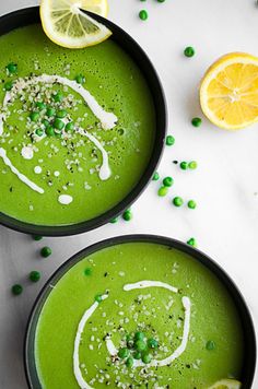 two black bowls filled with green soup and topped with peas, lemon slices and sprinkles