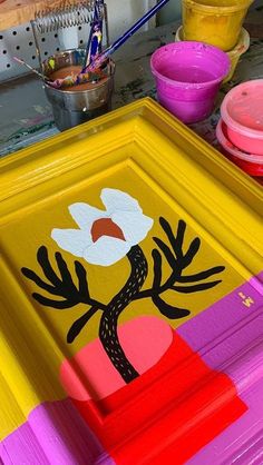 a yellow frame with flowers painted on it sitting next to other paints and containers in the background