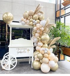 there is a white cart with balloons on it and some plants in the back ground