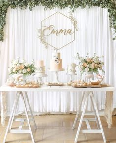 a table topped with cakes and desserts covered in greenery next to a white curtain