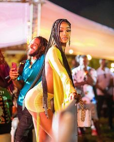 a woman in a yellow dress standing next to a man with dreadlocks on